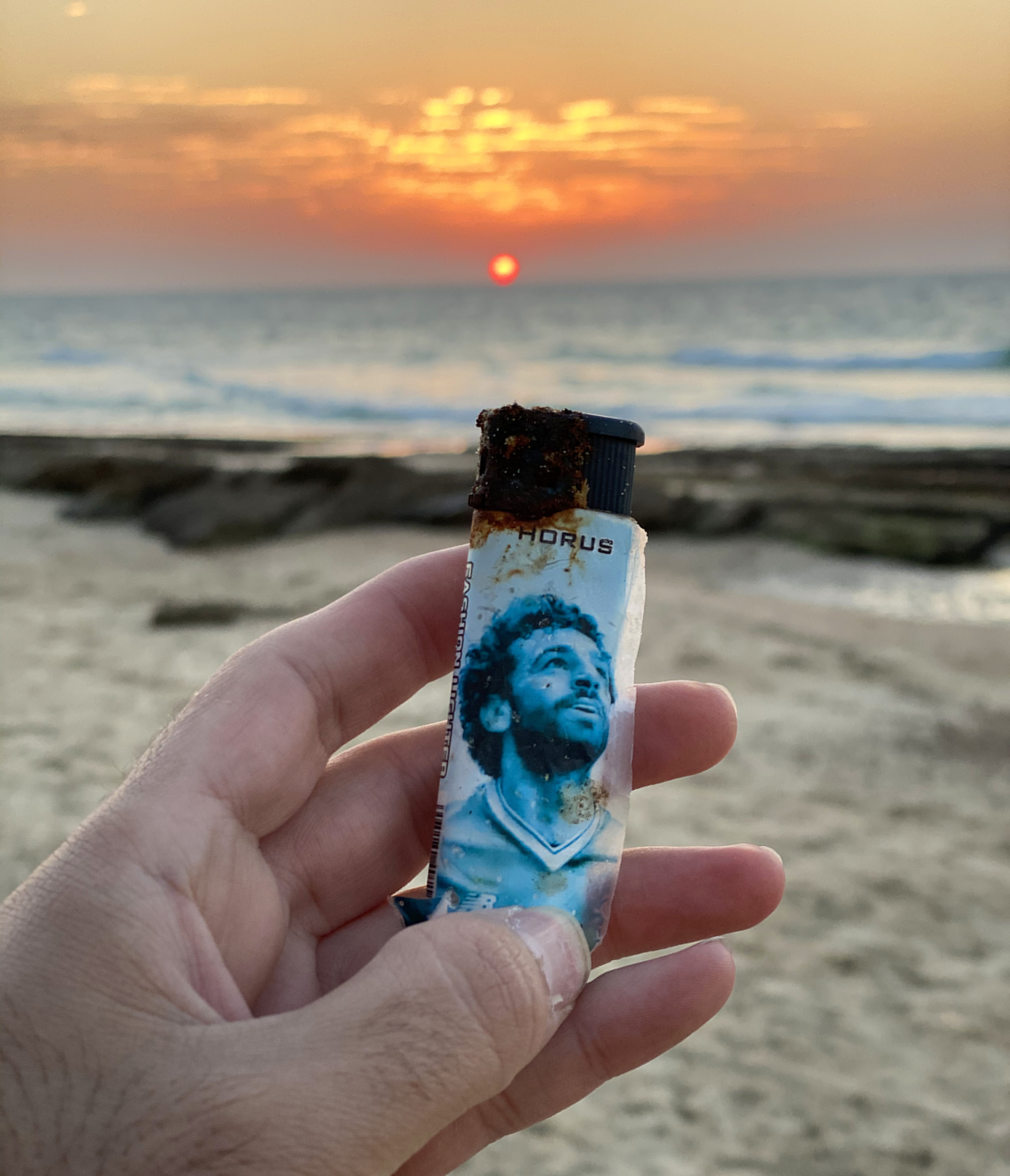 יד מחזיקה מצת חלודה על רקע שקיעה בים