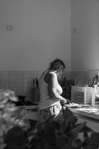 צילום בשחור לבן - אישה עומדת במטבח וחותכת ירקות על קרש חיתוך