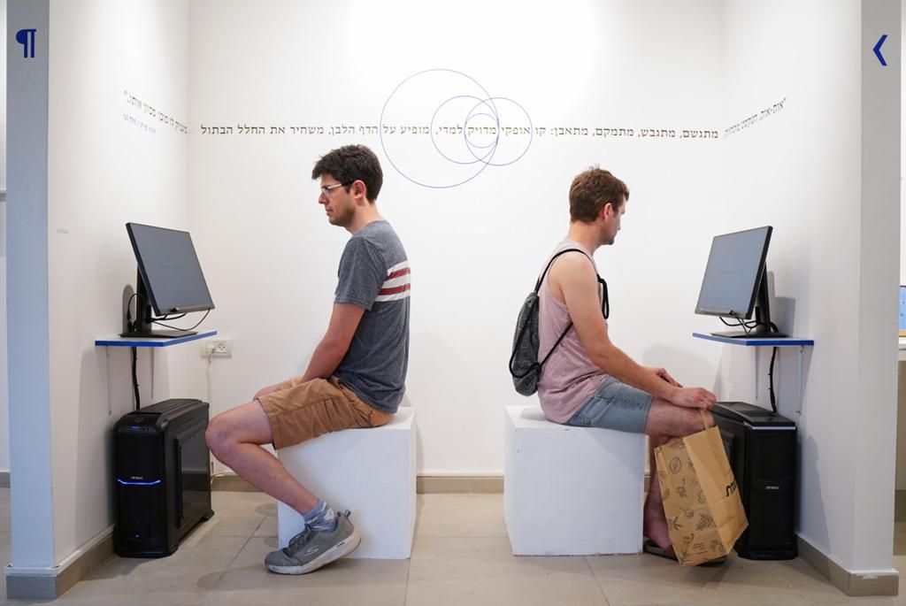 שני מבקרים בתערוכה מביטים בפרויקט של אלעד מדן
