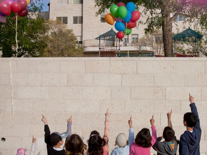 ילדים מרימים ידיים אל השמיים. בלונים באווי. פריים מתוך הסרט "מעיפים חומות"