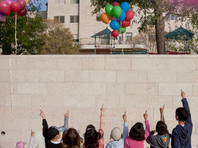 ילדים מרימים ידיים אל השמיים. בלונים באווי. פריים מתוך הסרט "מעיפים חומות"