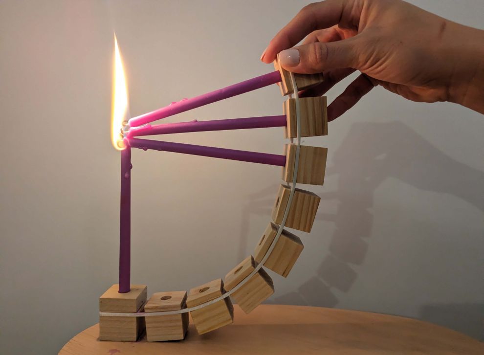 יד מקופפת את החנוכייה מפיסות עץ וגומיות ומדליקה נר