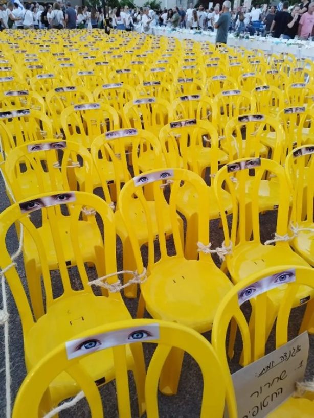 מיצג למען החטופים - כיסאות בצבע צהוב, עייניים מודפסות על הגב של הכיסאות